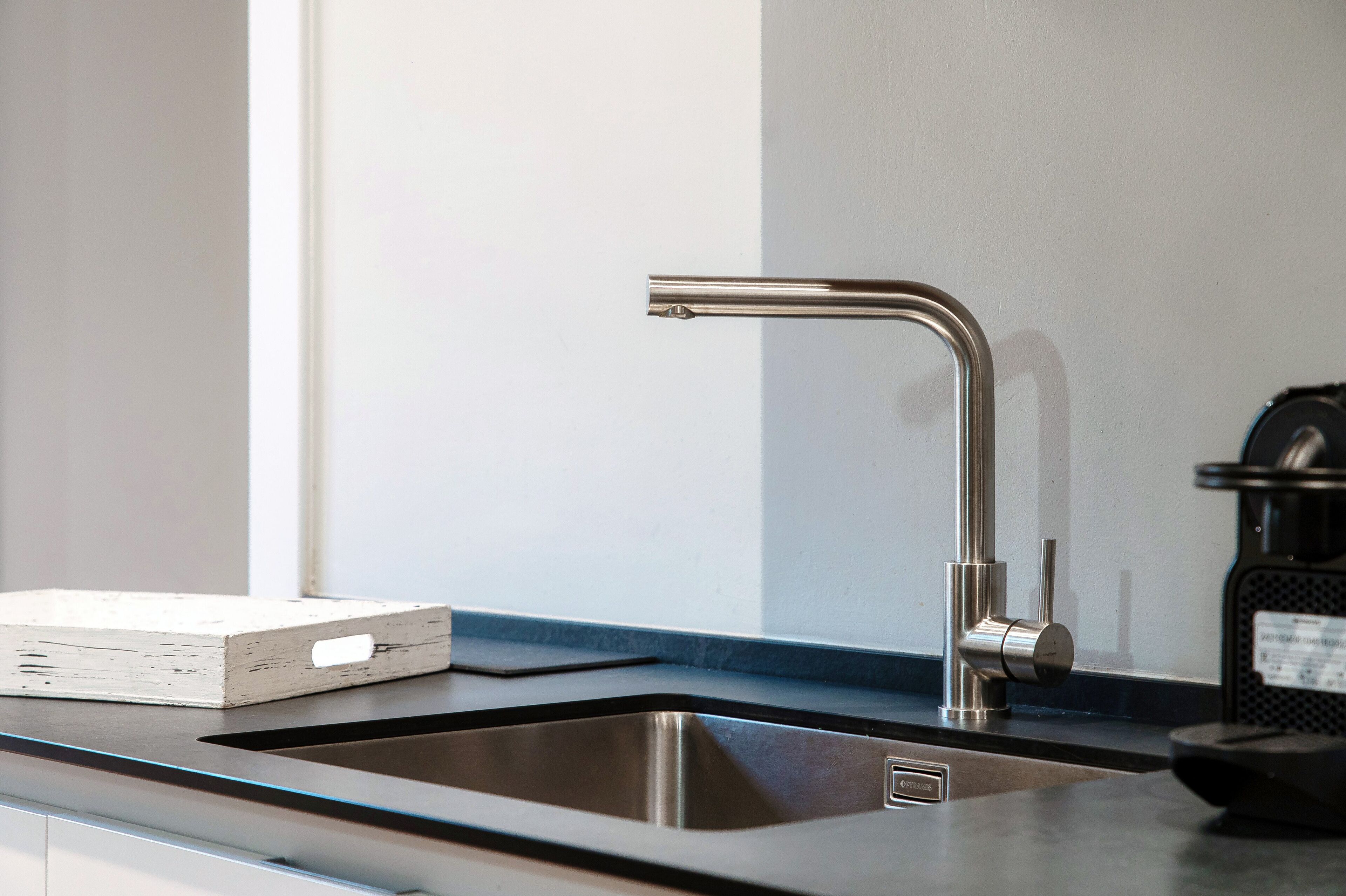 Una cocina moderna con un lavamanos de acero inoxidable, un caja blanca sobre la encimera y una cafetera negra.