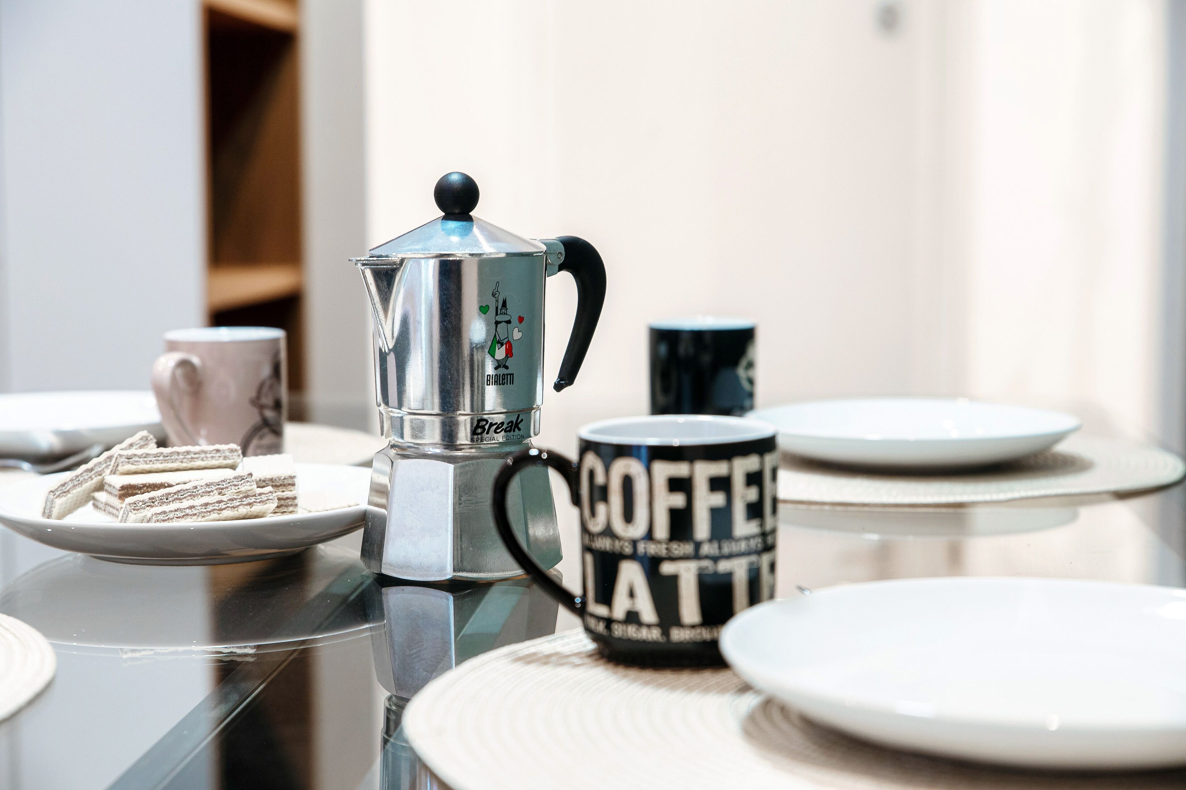 Una cafetera, una taza de café y un plato de sándwiches sobre una mesa.