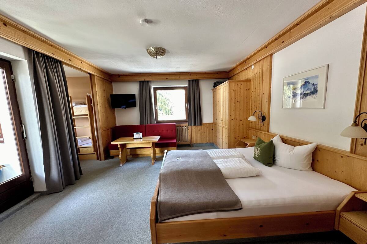 A wooden room with a bed, a red sofa, a table, and a TV.