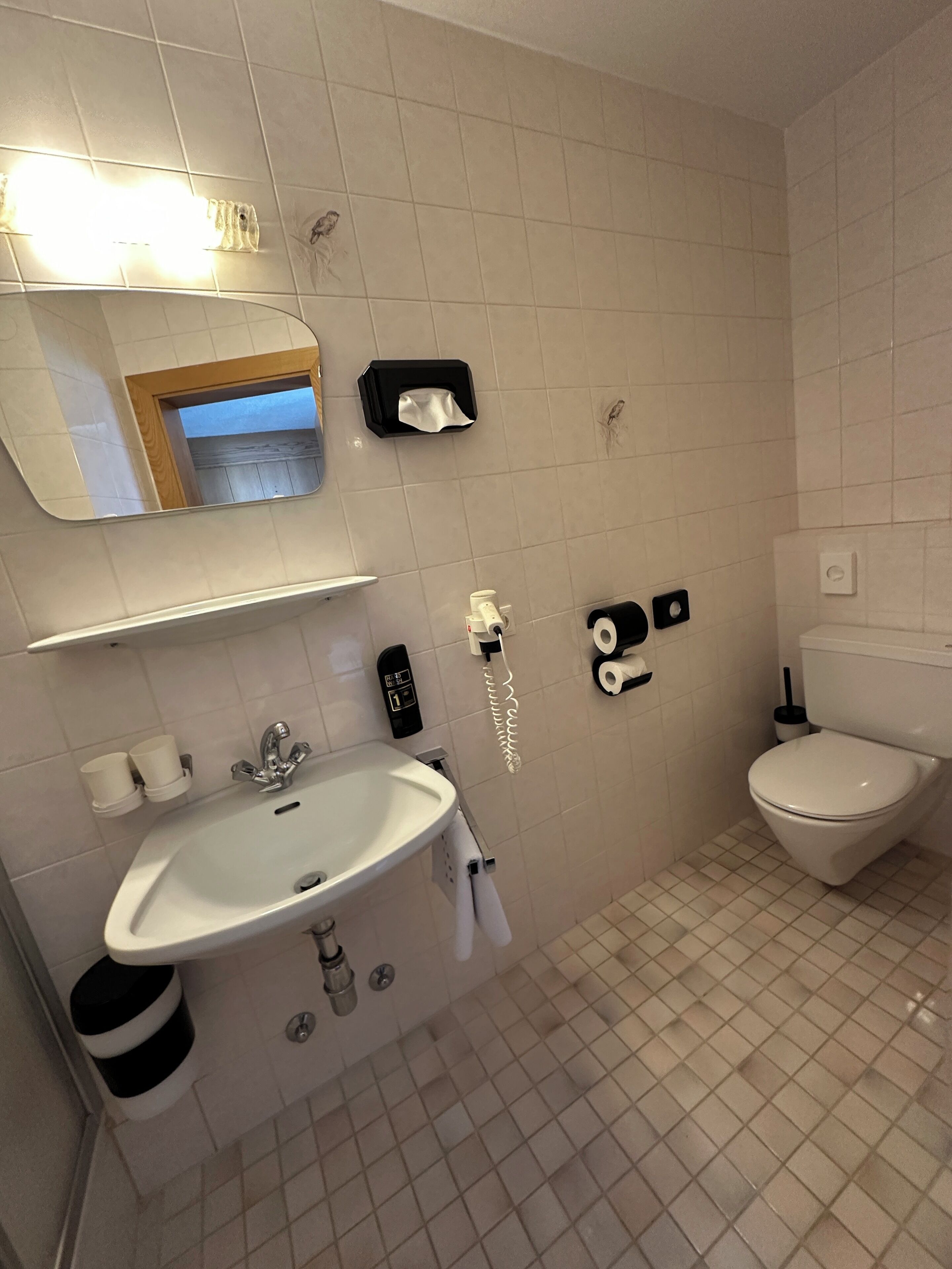 Un baño moderno con lavamanos, espejo, inodoro y secamanos.