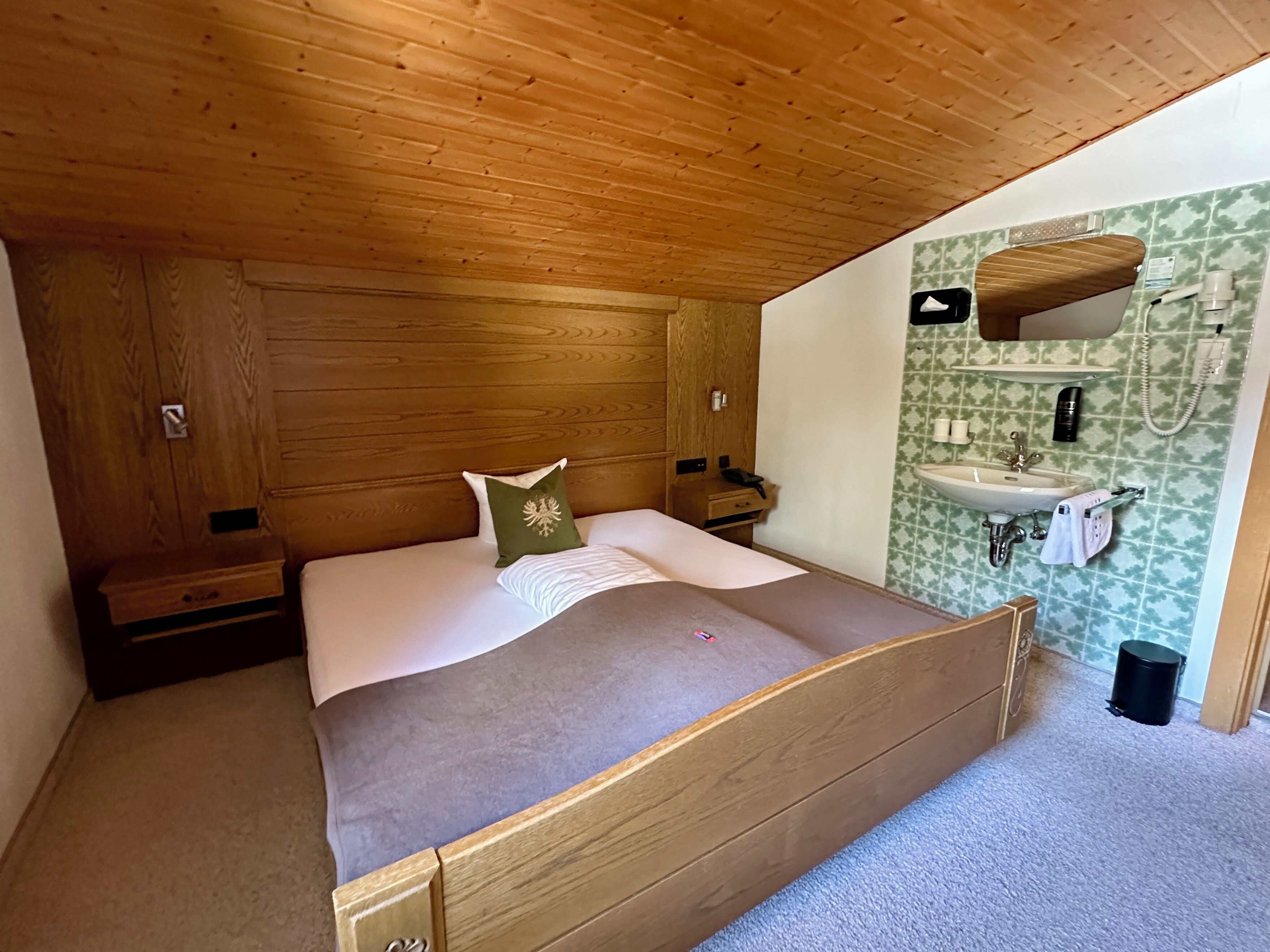 A bedroom with a wooden bed, a nightstand, a dresser, and a bathroom with a sink and mirror.