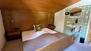 A bedroom with a wooden bed, a nightstand, a dresser, and a bathroom with a sink and mirror.