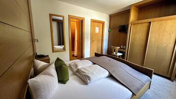 Een hotelkamer met een bed, een houten garderobe, een bureau met een stoel en een televisie.
