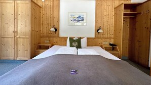 Une chambre d’hôtel avec des boiseries, un lit recouvert d’une couette blanche, deux tables de chevet avec des lampes et un tableau au mur.