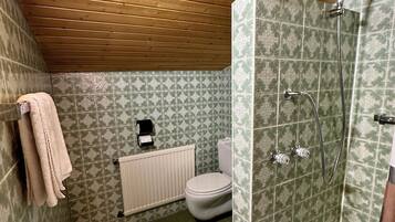Un baño con techo de madera, baldosas verdes con diseño, inodoro blanco, ducha con manguera y barra para toallas.