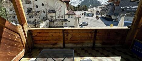 Un balcón con mesa y sillas, con vista a una calle con edificios y una montaña nevada al fondo.