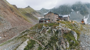 Un chalet de montagne avec une façade en pierre, une terrasse en bois et un drapeau indiquant qu’il est possible de skier.