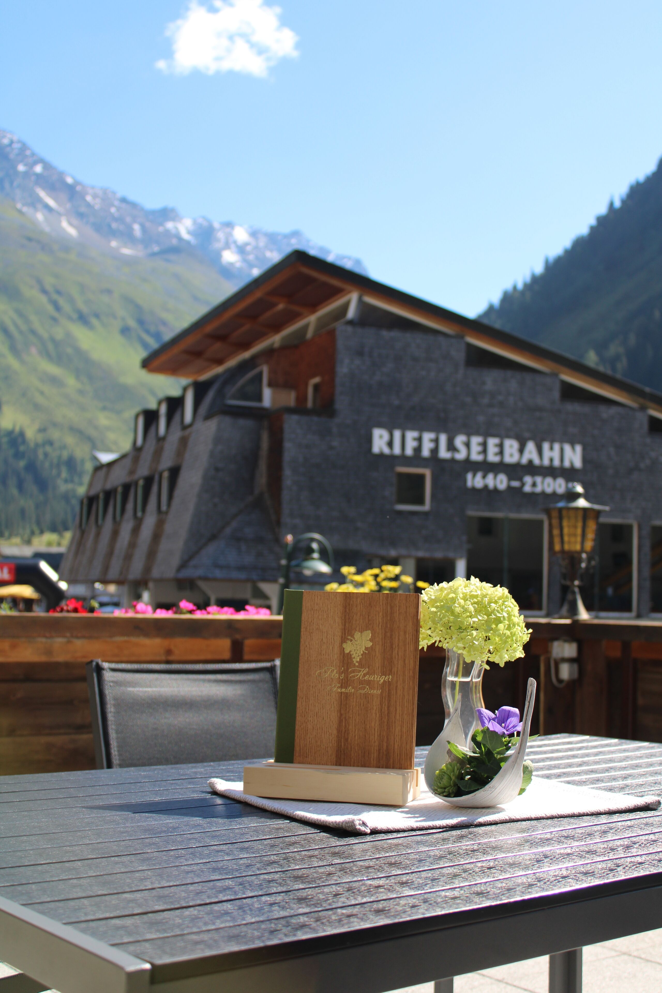 Taula amb un llibre i un vas amb flors, amb un paisatge de muntanyes i un edifici amb la inscripció "Riffelseebahn".