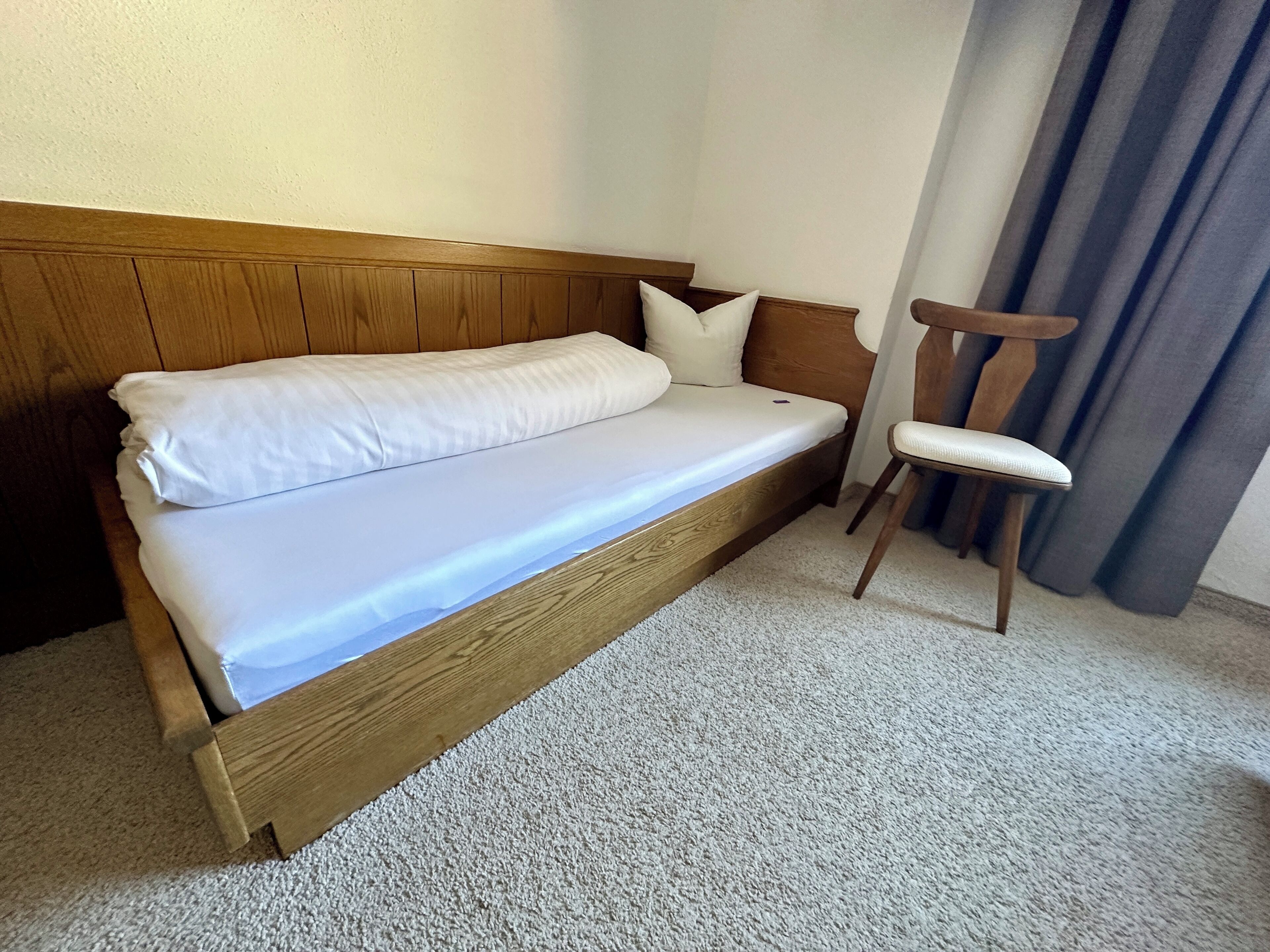 A single bed with a wooden headboard, a white mattress, and a wooden nightstand.