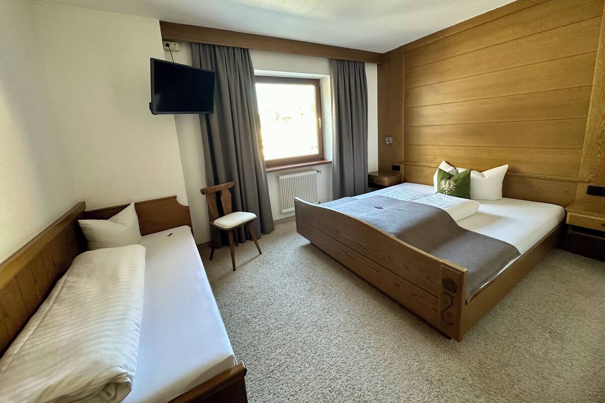 A hotel room with two beds, a TV, a window with curtains, and a wooden headboard.
