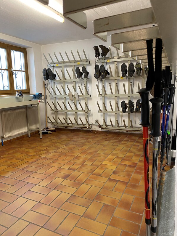A room with a tiled floor, a radiator, a window with bars, and a wall-mounted shoe rack with various shoes.