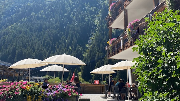 Une terrasse avec des sièges extérieurs, entourée de compositions florales et offrant une vue sur les montagnes.