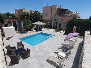 A swimming pool with lounge chairs and a table, surrounded by potted plants and a stone wall. - Apartment 2-Villa Augusta-del-Sol  (Fontane Bianche)