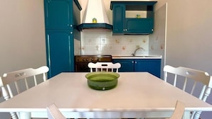A kitchen with teal cabinets, a white stove, and a white table with chairs. - Apartment 2-Villa Augusta-del-Sol  (Fontane Bianche)