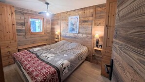 Een gezellig slaapkamer met houten wanden, een bed met een geborduurde sprei, twee nachtkastjes met lampen en een raam met uitzicht.