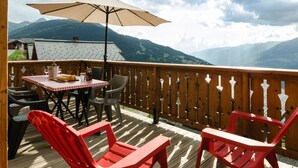 Een houten terras met een tafel, stoelen, een rode bank en een grote parasol.