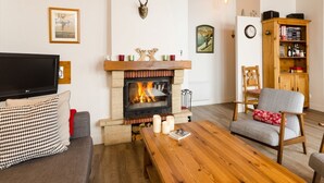 Een gezellige woonkamer met een open haard, een televisie en een comfortabele zithoek.