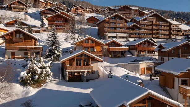 Een groepje houten chalets met balkons, gelegen voor een besneeuwde berg.