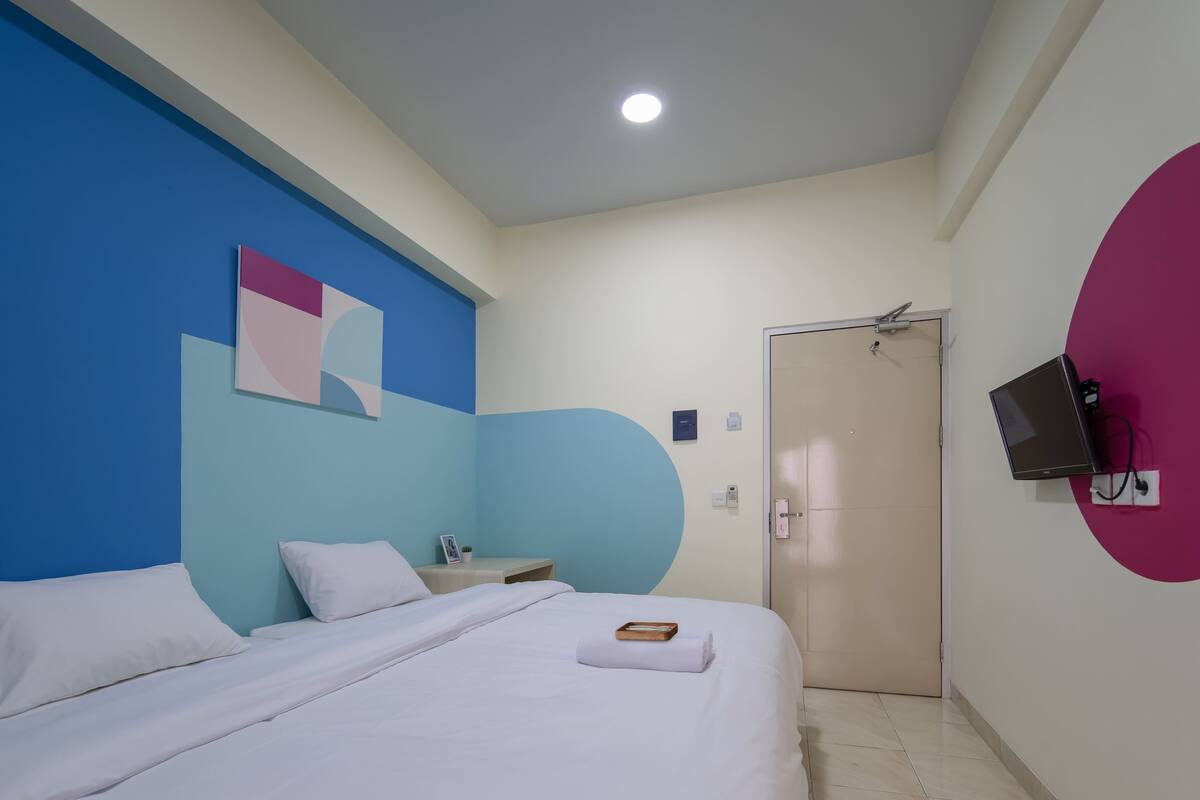 Une chambre d’hôtel avec un lit, une table de chevet, un téléviseur fixé au mur et une porte.