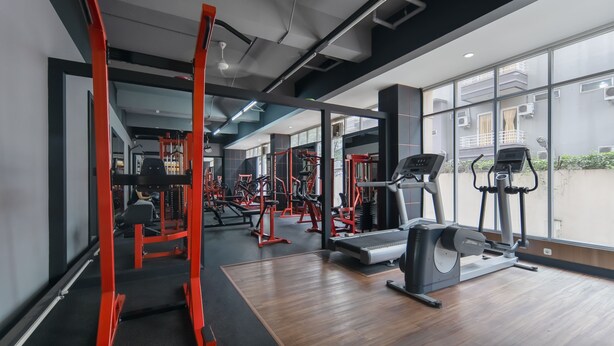 Een sportschool met diverse fitnessapparaten, grote ramen en een houten vloer.