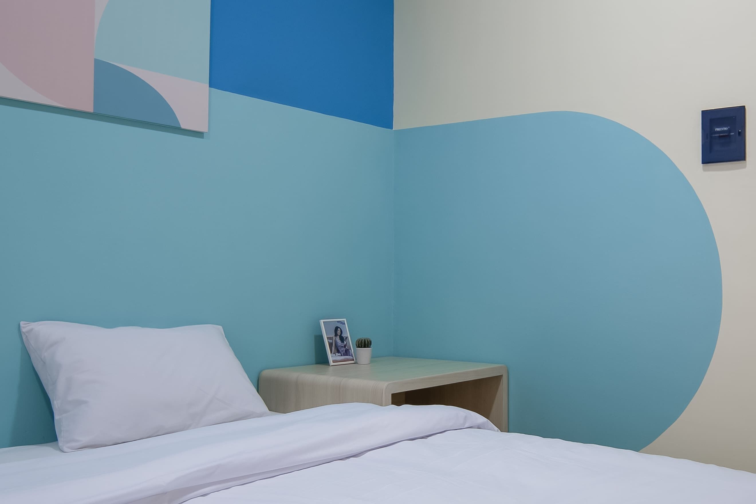 A bedroom with a bed, a bedside table, a small potted plant, and a framed photo.
