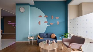 Een moderne woonkamer met een blauwe wand, een ronde houten salontafel, een blauwe bank en een roze fauteuil.