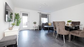 Ein modernes Wohnzimmer mit einer Couch, einem Esstisch mit Stühlen, einer Bank und einem kleinen Beistelltisch mit einer Pflanze.