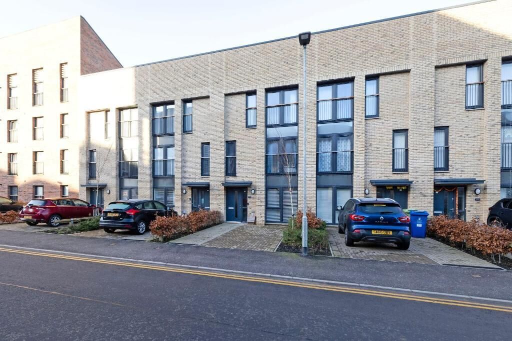 A multi-story residential building with a brick facade, multiple windows, and a parking area with cars.