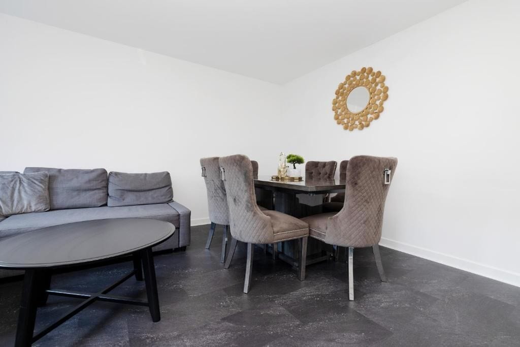 A modern living room with a grey sofa, a round coffee table, and a dining table with four chairs.