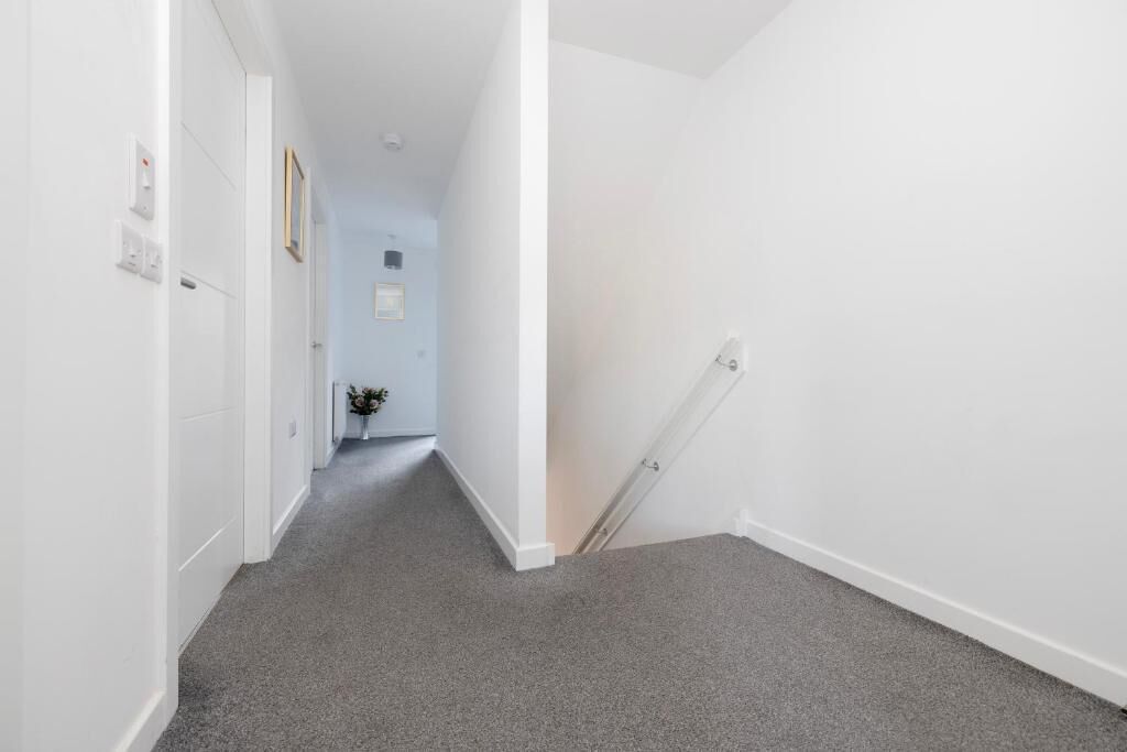 A narrow hallway with a carpeted floor and white walls.