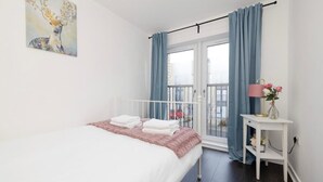 Ein Schlafzimmer mit Bett, Nachttisch mit Lampe, einem Bild an der Wand und Blick durch das Fenster.