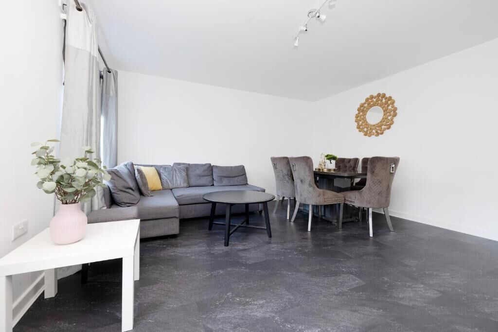 A modern living room with a grey sofa, a round coffee table, and a dining area with a small table and chairs.