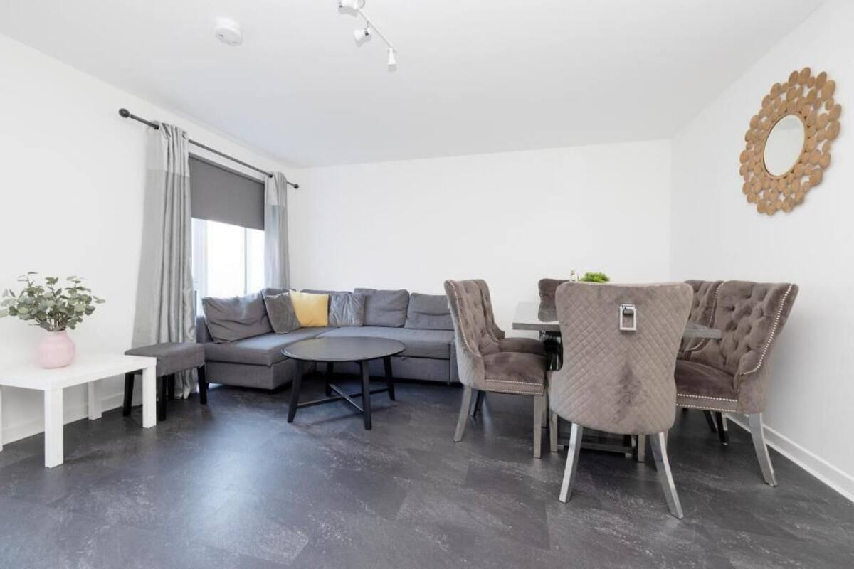 Una sala moderna con un sofá seccional gris, una mesa redonda y un comedor con una mesa pequeña y dos sillas.