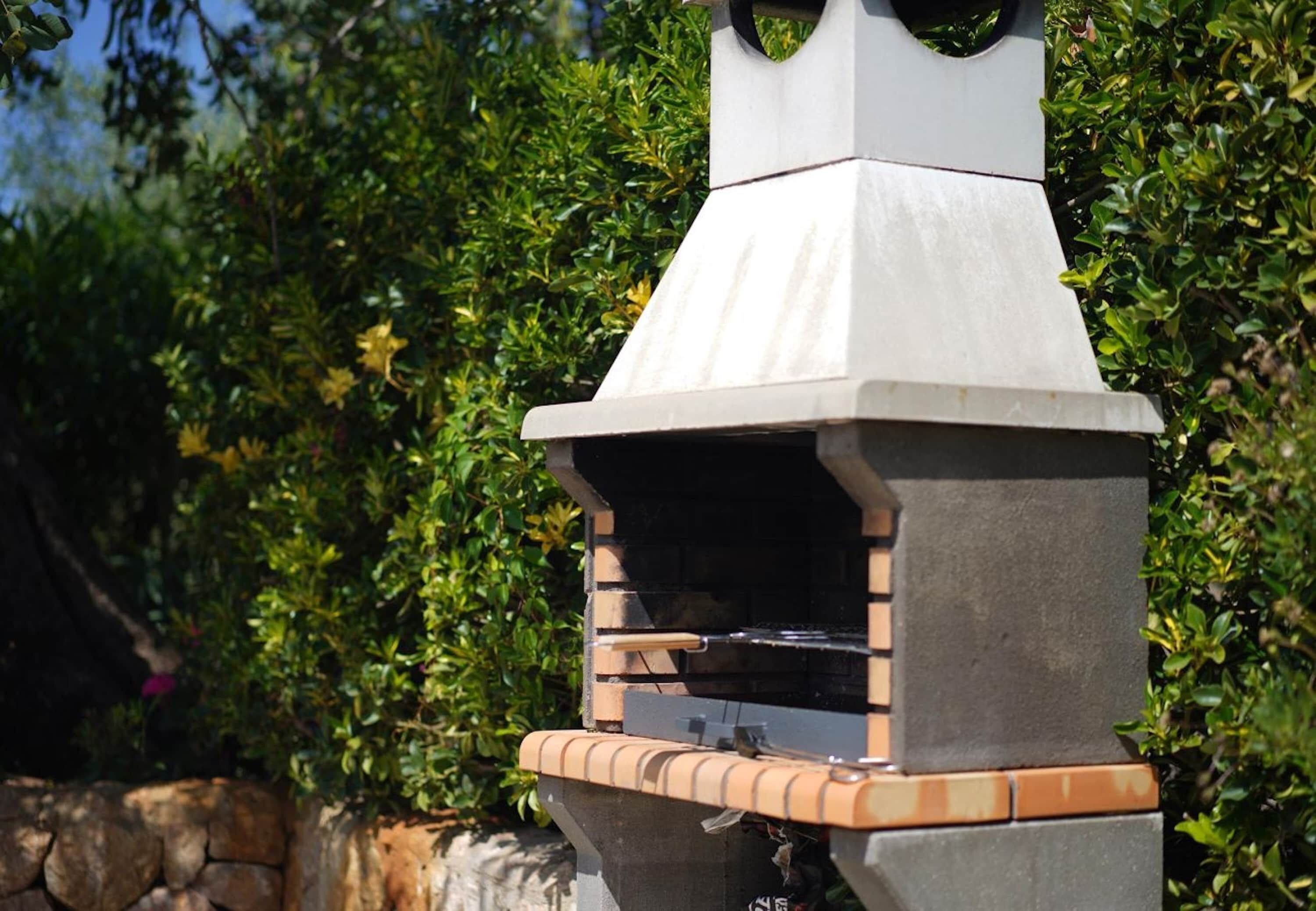 A barbecue grill with a chimney, set against a backdrop of green foliage.