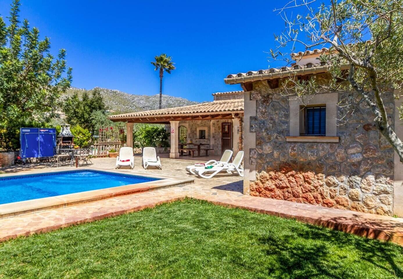 A pool with lounge chairs, a stone building, and a pergola.