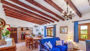 A spacious living area with a blue sofa, wooden dining table, and a kitchen in the background. - Villa Oliveres, Beautiful villa in the countryside near Pollensa (Pollença)