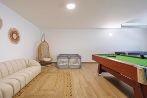 Una habitación con mesa de billar, un sofá, un tapete tejido y un sillón colgante.