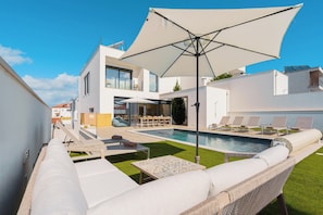 A modern outdoor pool area with lounge chairs, a table, and a large umbrella.