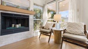 A living room with a fireplace, two chairs, a round side table, and a view of palm trees through large windows. - Gulf Views - Private Beach Access Across Street (Seacrest)