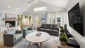 A spacious living room with a fireplace, a ceiling fan, and a large TV. - Gulf Views - Private Beach Access Across Street (Seacrest)