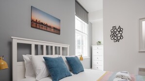 A neatly arranged bedroom with a bed, pillows, a bedside lamp, a window, and a motivational wall art piece.