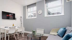 A modern living room with a dining area, grey walls, a flat-screen TV, and a large window.