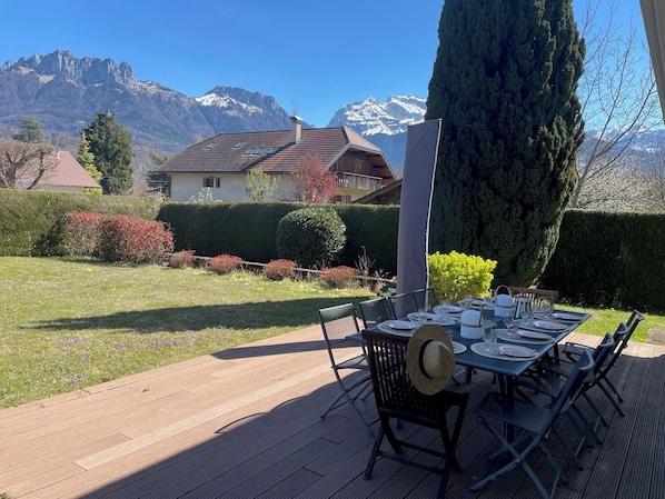 A deck with a table set for dining, surrounded by a well-maintained garden and a mountain view. - Maison de vacances à 300m du lac à Saint-Jorioz (Saint-Jorioz)