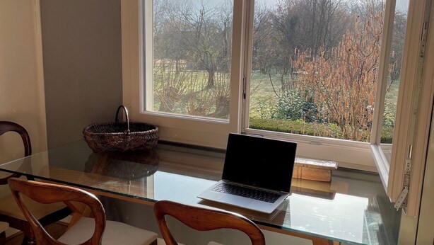 Un comedor con una mesa de vidrio, sillas de madera y una computadora portátil.