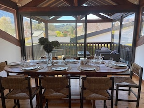 A dining area with a table set for six, surrounded by wicker chairs, with a view of a residential area through large windows. - Maison de vacances à 300m du lac à Saint-Jorioz (Saint-Jorioz)