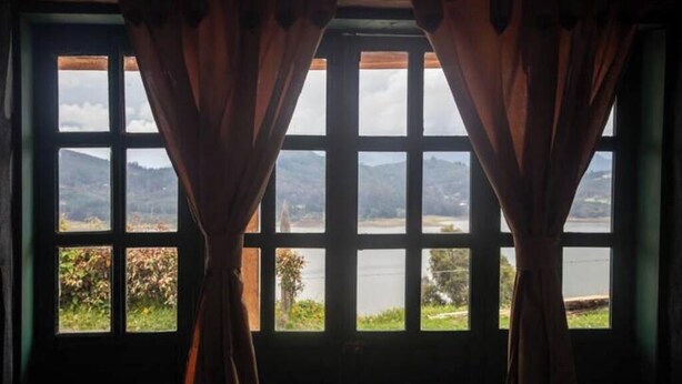 A room with a large window featuring a view of a lake and mountains. - Viewpoint of the waters (Sesquilé)