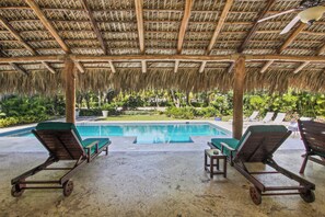 Zona de piscina techada con sillones de descanso y vista a una piscina.