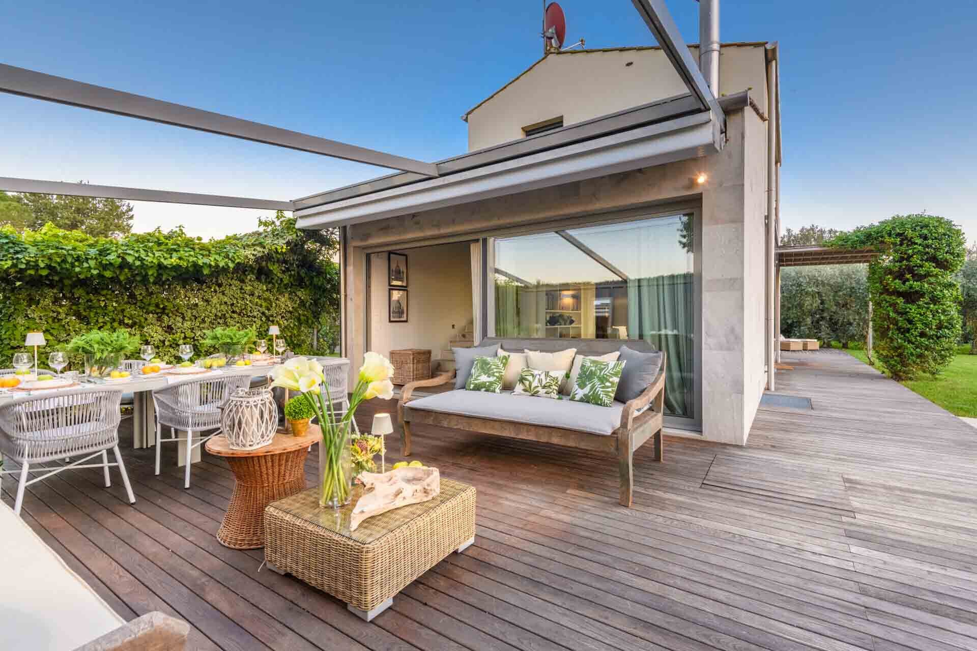 A modern outdoor patio with a dining area, a sofa, and a wooden deck.