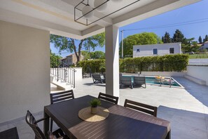 Un patio con mesa, sillas y vista a una piscina y el paisaje circundante.