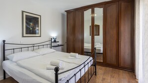 Een keurig opgemaakt bed met witte lakens, een houten garderobe en een ingelijste foto aan de muur.